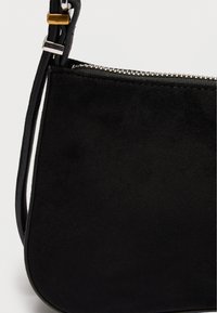 Geantă de umăr din piele întoarsă neagră, cu fermoar argintiu și curea reglabilă decorată cu accente metalice aurii și argintii.