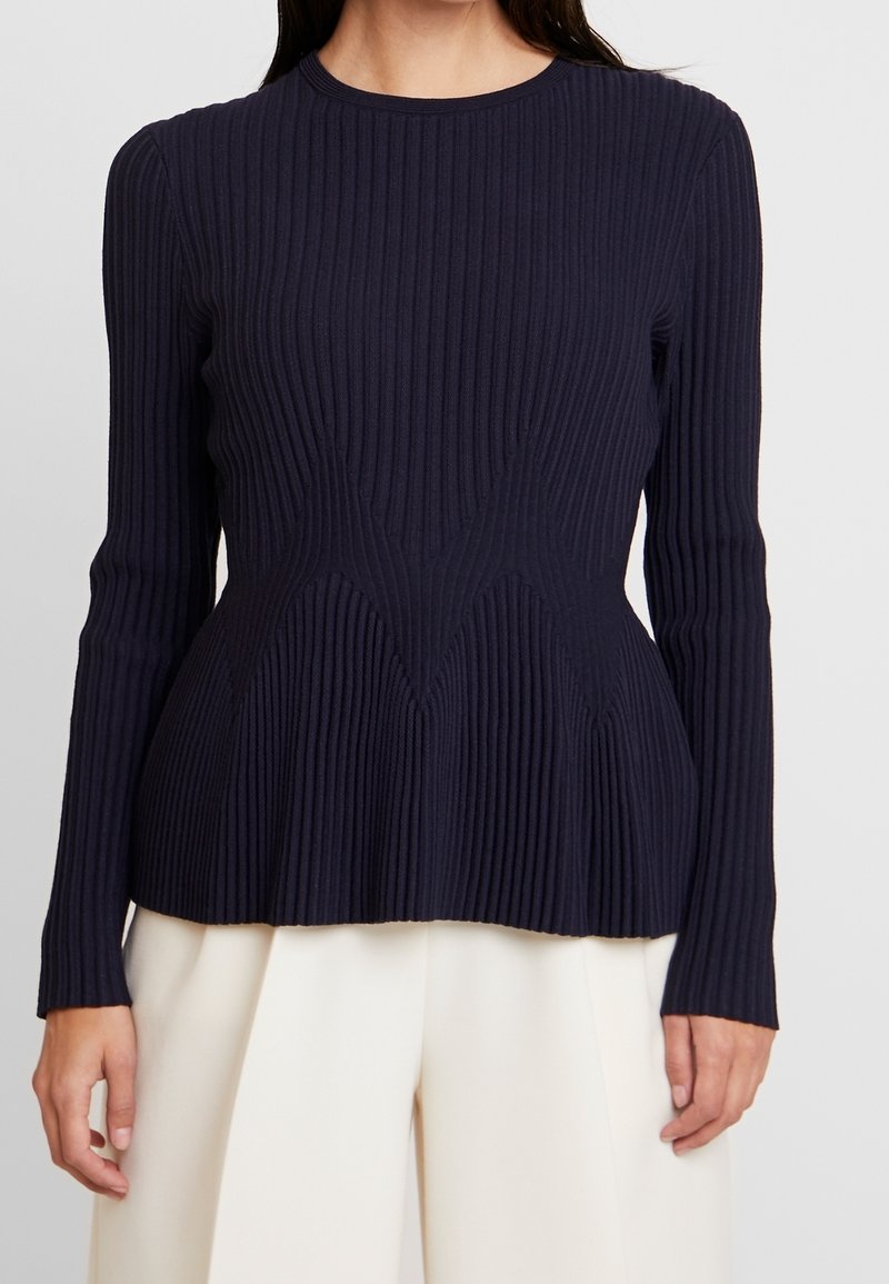 Tumma laivastonsininen ribbineulottu pitkähiha-pusero pyöreällä pääntiellä, jossa on vartalonmyötäinen leikkaus ja hienovarainen tekstuuri, valmistettu pehmeästä kankaasta.
