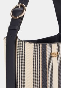Borsa a secchiello in tela a strisce con un motivo beige e navy, caratterizzata da un logo in tono oro, una tracolla in pelle e un accento in hardware circolare.