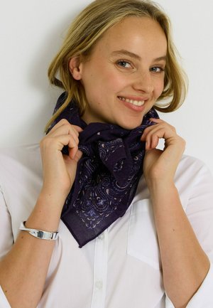 Bufanda morada oscura con patrón de paisley, llevada de manera suelta alrededor del cuello. Hecha de un tejido ligero, con una textura suave y bordes limpios.