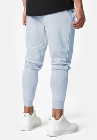 Himmelblaue, enganliegende Jogginghose mit elastischen Bündchen und Seitentaschen, aus weichem Material. Kombiniert mit weißen Sportschuhen.