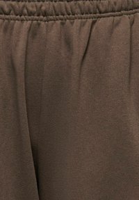 Tissu marron avec taille élastique froncée, montrant une texture douce et de légères plis dans le matériau.