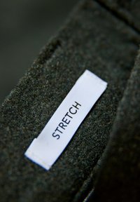 Czarna tkanina o miękkiej fakturze, na której wyraźnie widoczna jest biała metka z napisem "STRETCH". Skupienie na materiale i detalach wzornictwa.