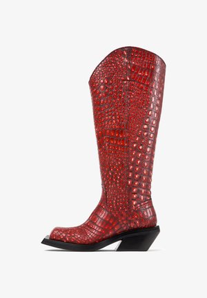 Botte de cowboy rouge haute avec texture crocodile en relief et talon noir incliné, vue de côté sur fond blanc.