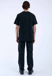 Camiseta de algodón negra con un corte relajado, mangas cortas y dobladillo recto, combinada con pantalones negros y calzado negro.