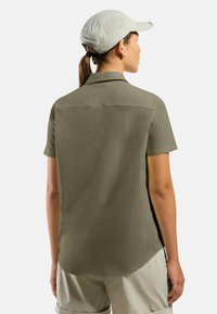 Korte mouwen olijfgroene shirt met een gestructureerde afwerking en een afgeronde zoom, gecombineerd met lichte shorts en een lichte pet.