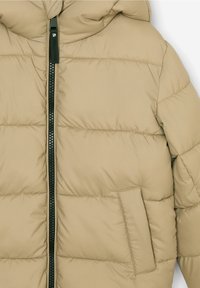 Beige polstret jakke med lynlås, prydet med syede vandrette paneler og en enkelt sidelomme. Glat, let materiale.