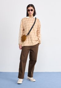 Beige patterned long-sleeve shirt with a white collar, brown trousers, and cream sneakers. Includes round brown crossbody bag and sunglasses.