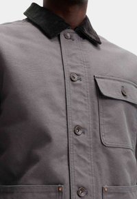 Grå lærredjakke med kordfløjskrave, metalknapper, en stikklap lomme og et struktureret design. Glat tekstur med slidstærkt stof.