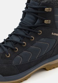 Dark blue hiking boot made of textured fabric and suede, featuring metal lace eyelets, a rubber sole, and a distinctive chevron pattern.