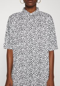 Chemise noire et blanche à manches courtes présentant un motif de léopard, un col boutonné et une coupe décontractée. Tissu lisse et léger.