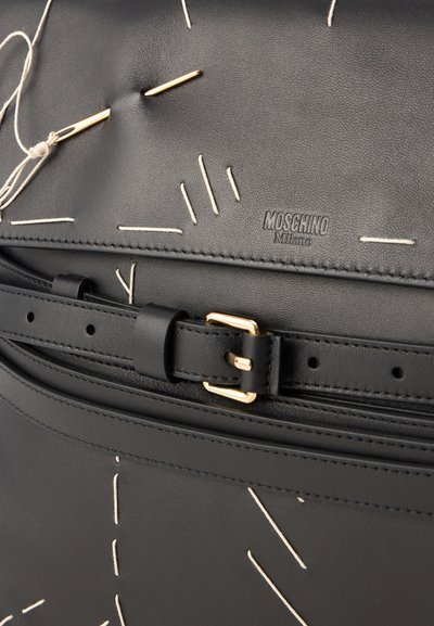 Borsa in pelle nera con cuciture bianche, una fibbia dorata e il logo Moschino embossato sulla superficie. Gli elementi di design unici includono un motivo cucito.