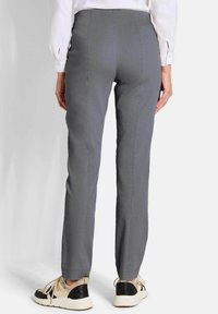 Grijze, op maat gemaakte broek met een slim fit, voorzien van details in de achternaad. Gekozen voor lichtgekleurde sneakers en een wit shirt met lange mouwen.