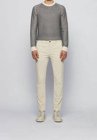 Pull en maille grise avec des accents crème, associé à un pantalon chino crème et des chaussures beige clair. La tenue présente une coupe moderne et des lignes épurées.