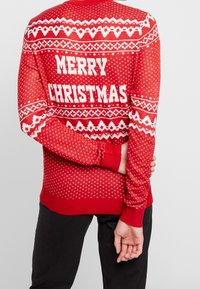 Rode gebreide trui met witte tekst "MERRY CHRISTMAS" op de achterkant, geometrische patronen en geribbelde manchetten, zoom en halslijn.