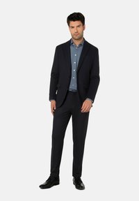 Marineblauer Anzug aus strukturiertem Stoff, einreihiger Blazer und Slim-Fit-Hosen, kombiniert mit einem hellblauen Hemd und schwarzen Schuhen.