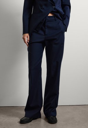 Navy-Hosen aus einem glatten Stoff, mit einer taillierten Passform und geradem Bein, dezenten Falten und Seitentaschen. Schwarze Slipper runden den Look ab.