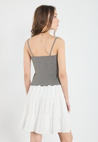 Grå ribbestrikket topp med tynne stropper og bølget kant, kombinert med en hvit laget skjørt med teksturert stoff. Rent, minimalistisk design.