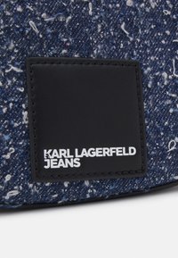 Džínová taška v námořnické modři s flekatou texturou, která má černý kožený štítek s bílým nápisem "KARL LAGERFELD JEANS".