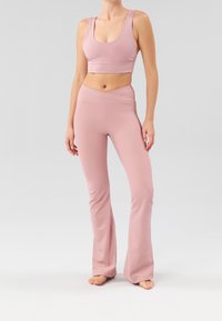 Lichtroze sportset bestaande uit een crop top met ronde hals en nauwsluitende, uitlopende broek met een geribbelde structuur en een overslag tailleband.