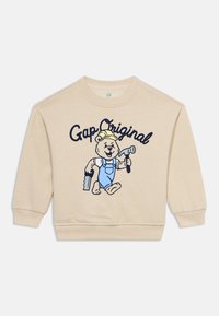 Μπεζ παιδικό φούτερ με καρτούν αρκούδα σε μπλε σαλοπέτα που κρατά ένα σφυρί και ένα πριόνι, με κείμενο "Gap Original" από πάνω.