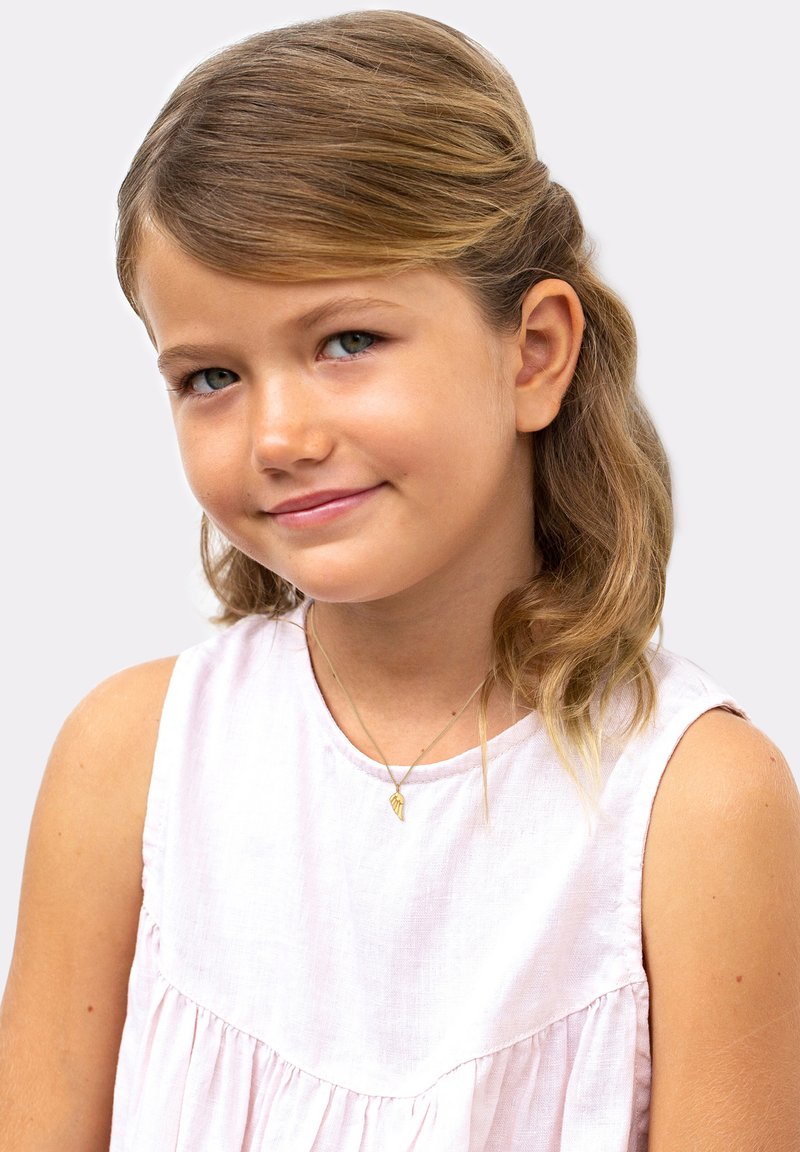 Barn iført en lys pink, ærmeløs linnedkjole med en volangkant. Enkel guld-halskæde med vedhæng. Glat, bølget blond hår.