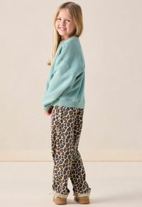 Sweatshirt bleu clair avec épaules déchues associé à un pantalon beige à imprimé léopard. Chaussures chunky beiges et cheveux lisses et droits.