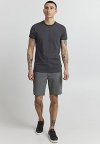 T-shirt gris avec un col noir contrastant, associé à un short gris foncé. La tenue présente une coupe décontractée et un design simple.