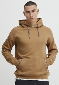 Felpa marrone con tasca frontale a marsupio, cappuccio regolabile con stringhe e cordino a contrasto nero e bianco, realizzata in tessuto morbido.