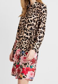 Robe chemise à manches longues imprimée léopard, tissu cintré à la taille, avec un bas floral composé de roses roses et rouges avec des accents bleus.