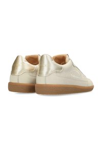 Sneaker bianche in pelle con un accento dorato a forma di onda sul tallone, suola in gomma marrone e design minimalista. Texture liscia con branding sottile.