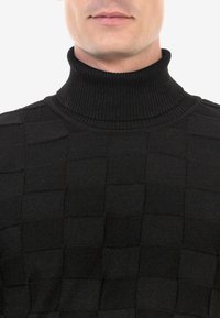 Zwarte coltrui met een gestructureerd ruitpatroon, geribbelde halslijn en gladde stof, die de gestructureerde vorm benadrukt.