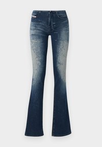 Jeans de mezclilla acampanados con un lavado azul oscuro y un ligero desvanecimiento, superficie texturizada y cremallera. Diseño de cinco bolsillos con etiqueta de la marca.