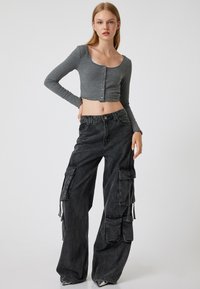 Top corto a maniche lunghe grigio a costine con bottoni, abbinato a pantaloni cargo neri larghi con più tasche e una vestibilità comoda.
