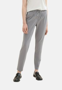 Graue maßgeschneiderte Hose mit glatter Textur, Kordelzugbund und schmaler Passform, kombiniert mit schwarzen Schnürschuhen. Minimalistisches Design, ohne Muster.