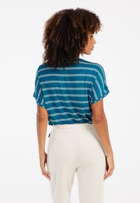 Tamsiai mėlynos ir žalios dryžuotos marškinėliai turi trumpas rankoves ir laisvą siluetą, derinami su kreminės spalvos, minkštais, elastiniu juosmeniu kelnių.