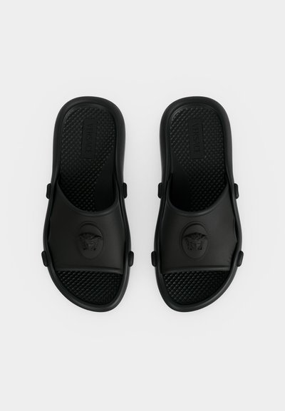 Paire de sandales noires Versace slip-on avec semelles texturées et emblème tête de Méduse sur les brides, vues de dessus sur fond blanc.