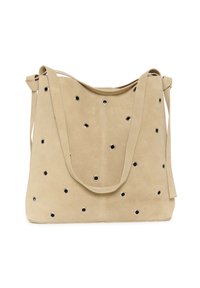 Sac à bandoulière en daim beige avec plusieurs œillets en métal et une longue sangle, forme rectangulaire légèrement souple.