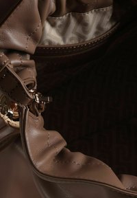 Intérieur de sac à main en cuir marron avec texture lisse, accessoires dorés et doublure subtilement imprimée. Tissu bien structuré et coutures visibles.