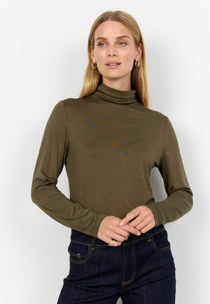 Haut à col roulé à manches longues de couleur olive, fabriqué en tissu lisse, avec un design minimaliste et une coupe ajustée. Associé à un jean en denim foncé.
