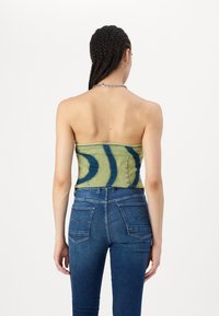 Top senza spalline in denim verde con motivi astratti blu, forma aderente. Abbinato a jeans blu a vita media con doppie tasche posteriori.
