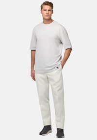 T-shirt gris clair à manches courtes, associé à un pantalon blanc et des baskets noires. Design simple avec une coupe décontractée, couleurs unies.