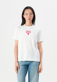 White cotton t-shirt featuring red "JOOP! JEANS" graphic and heart design on the chest, paired with light blue denim jeans.