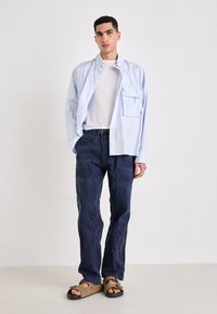 Lichtblauwe gestreepte overhem, witte T-shirt eronder, donker marineblauwe losse cargo broek en bruine platte sandalen. Minimalistisch ontwerp, casual stijl.