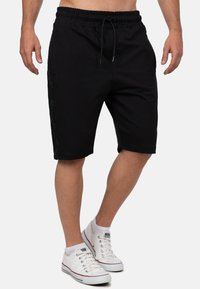 Shorts en coton noir avec une taille élastique, des rayures latérales et des poches. Assortis à des baskets blanches. Tissu texturé avec une coupe décontractée.