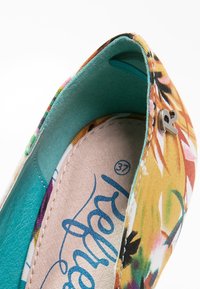 Chaussure plate colorée à motif floral montrant un extérieur en tissu, une doublure intérieure turquoise, une semelle intérieure beige avec écriture bleue et une lettre métallique "R" sur le devant.