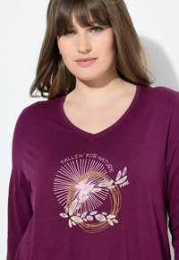 Lila Langarmshirt mit V-Ausschnitt, verziert mit einem Blattmuster und dem Text "FALLIN' FOR NATURE" in Weiß und Rosa.