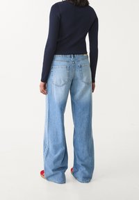 Vaqueros de pierna ancha en azul claro con un acabado desgastado, cinco bolsillos y cintura alta. Combinados con un top ajustado de manga larga en azul marino.