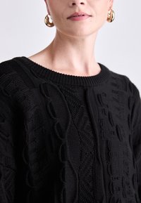 Black knit sweater featuring textured patterns, a wide round neckline, and ribbed cuffs. Simple design emphasizes fabric details and structure.