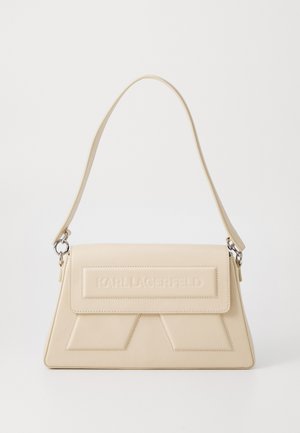 Bolso de mano de cuero beige con un diseño estructurado, logotipo en relieve en la parte frontal, correa ajustable y acentos angulares en el cuerpo.